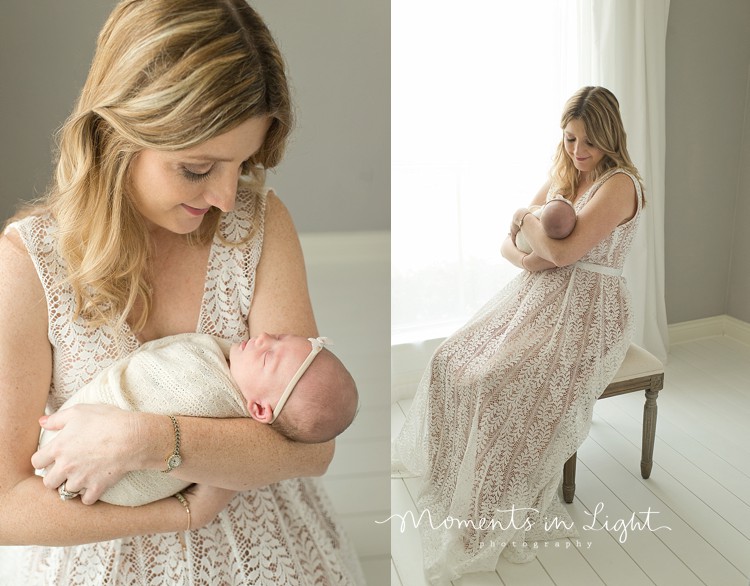mom holding newborn baby girl wearing white dress by window