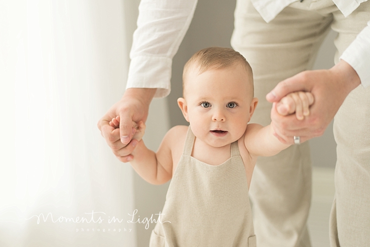 baby boy wearing cream romper walking holding dad's hands in Houston photo studio